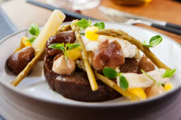 Tellergericht A-ROSA Sylt Ein Teller mit einem raffieniert angerichtetem Gericht, dahinter ist eine Gabel und ein Messer zu sehen.