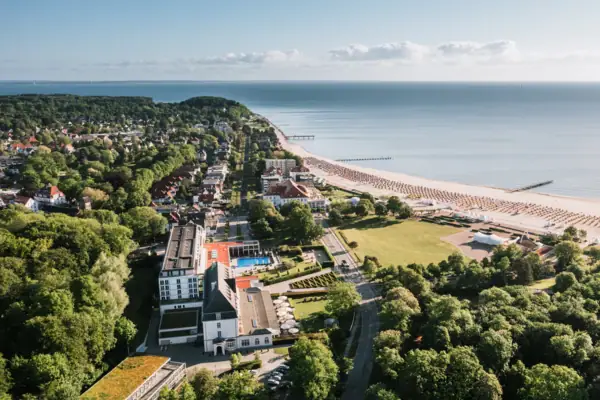 Luftaufnahme vom A-ROSA Travemünde mit dem Strand, der Ostsee und Bäumen.