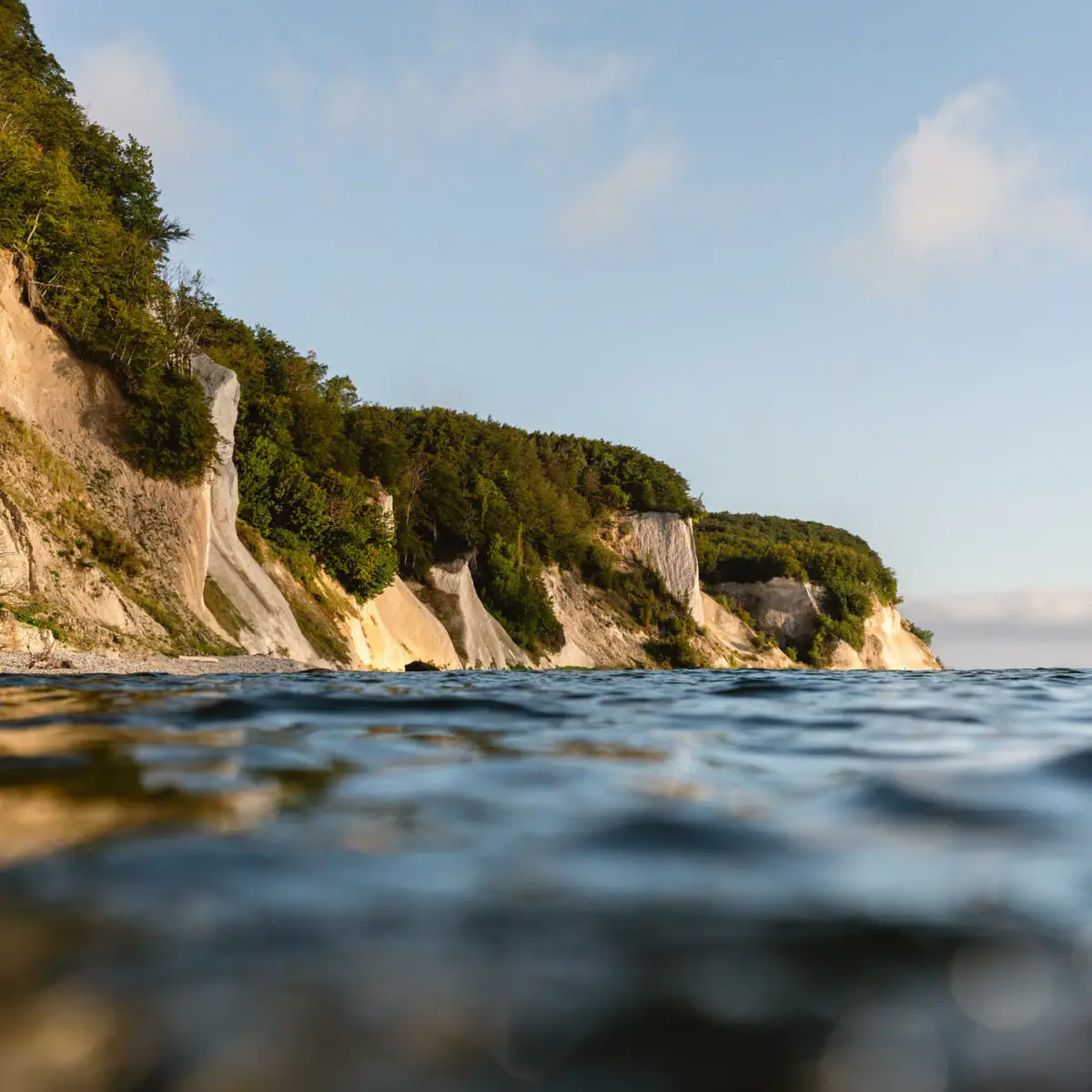 Gewässer mit Klippe und Bäumen im Vordergrund.