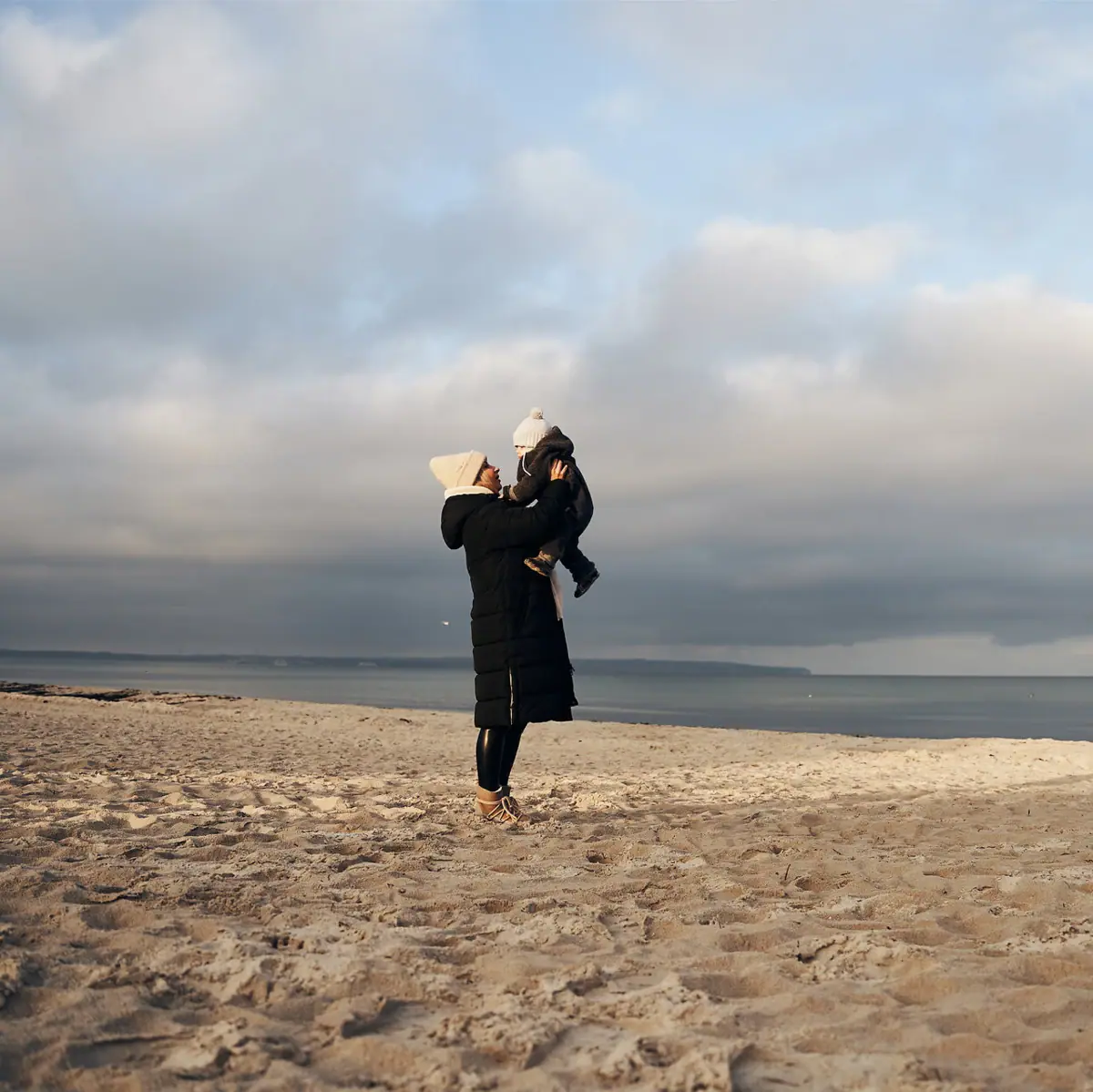 Una donna tiene in braccio un bambino sulla spiaggia.