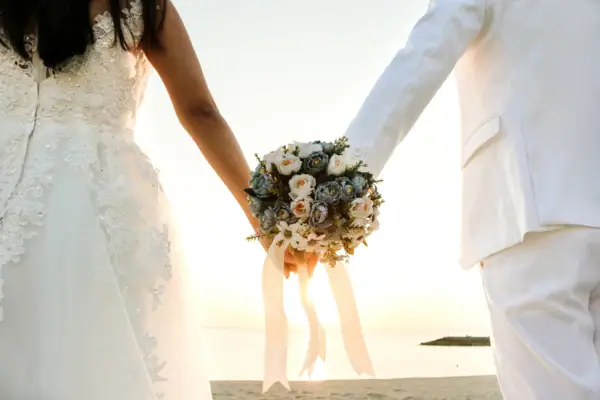 Ein Mann und eine Frau halten sich an den Händen, die Frau trägt ein Hochzeitskleid.