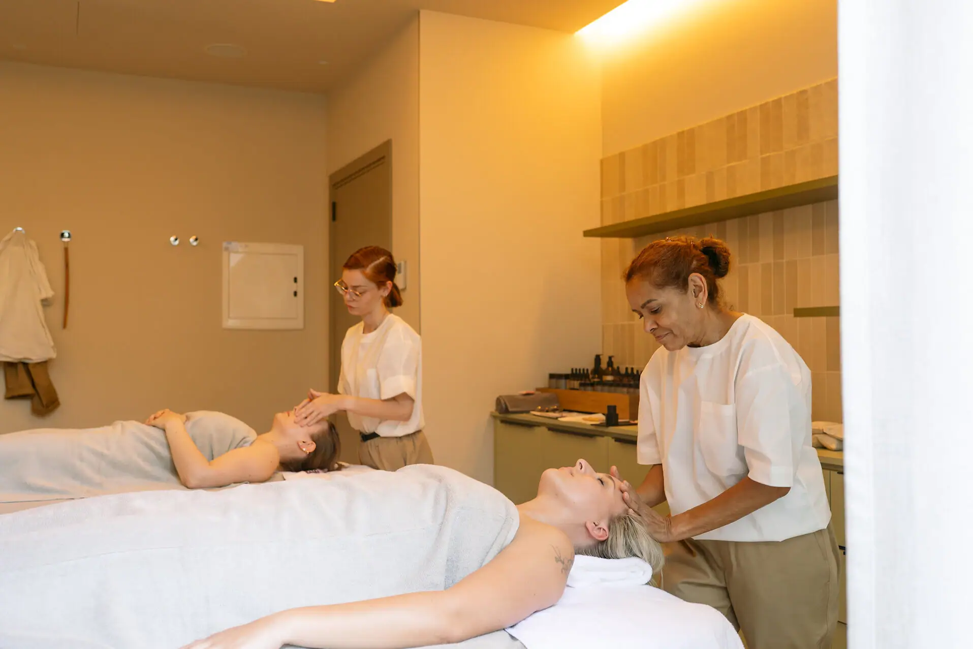 Frauen genießen eine Massage, betreut von zwei Therapeutinnen im Wellnessbereich.