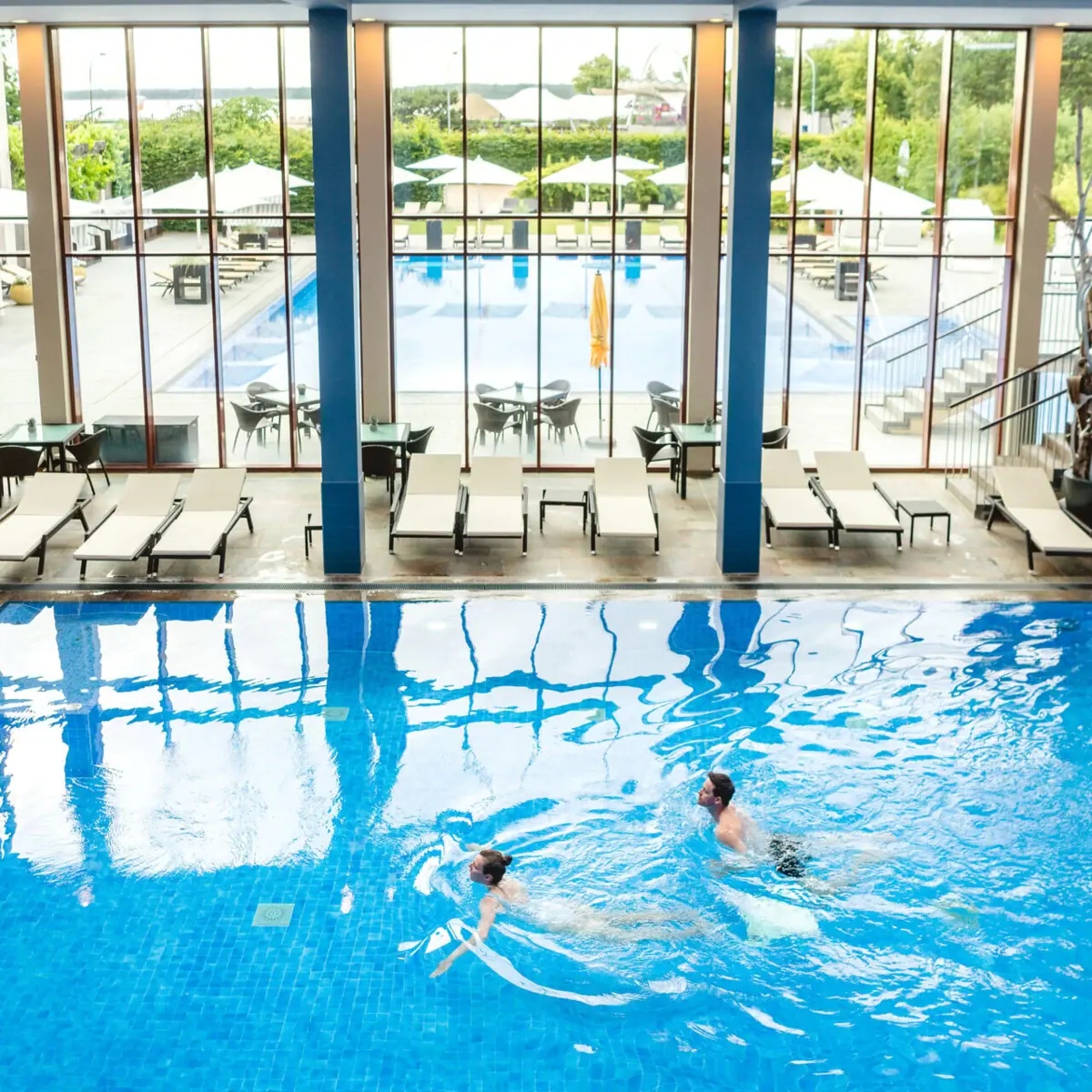 Piscina coperta all’A-ROSA Travemünde Un uomo e una donna nuotano in una piscina.
