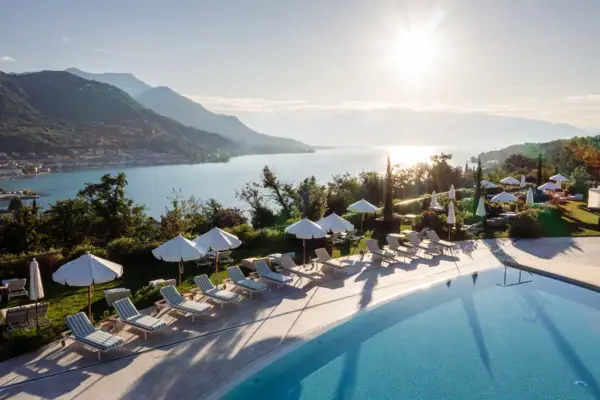 Blick über den Poolbereich des A-ROSA Gardasee mit Sonnenschirmen und Panoramablick auf den See und die Berge.