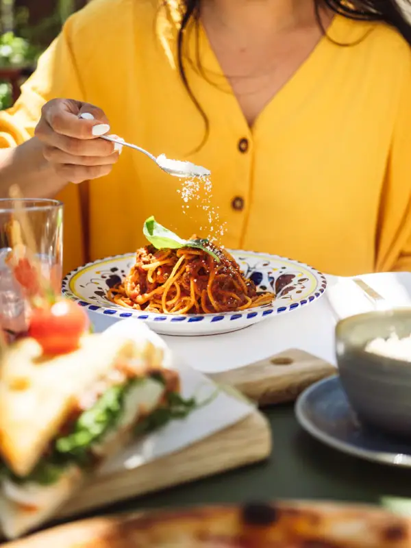 Persona che versa sale su un piatto di spaghetti.