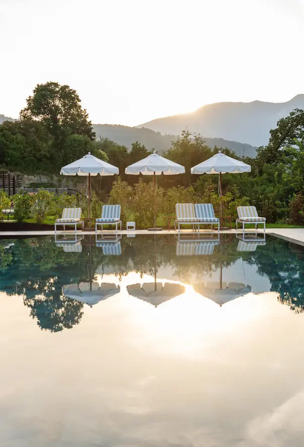 Una piscina con lettini a righe e un paesaggio verde sullo sfondo 