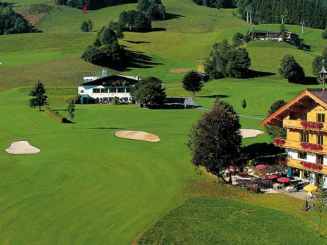 Campo da golf con edificio e trappola di sabbia, circondato da alberi e prati.