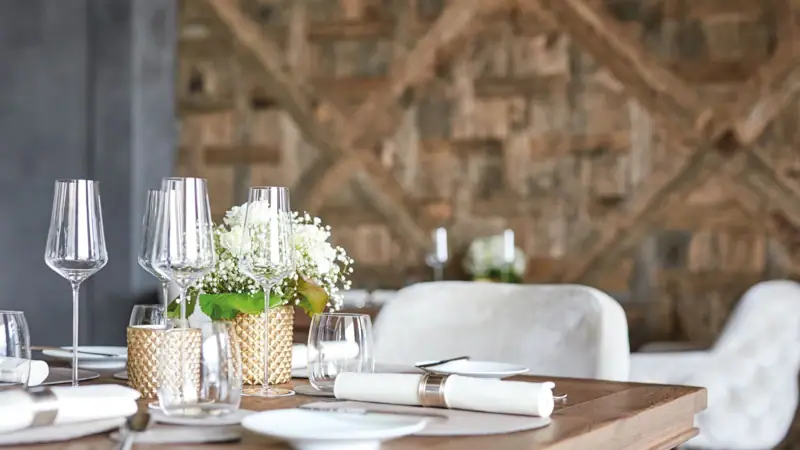 Ein Tisch mit Weingläsern und Blumenarrangement vor einer Holzvertäfelung..