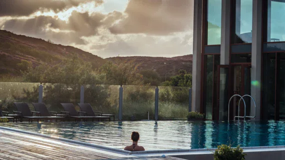 Donna che nuota in una piscina esterna con montagne sullo sfondo.