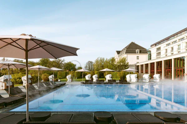 Piscina esterna di un resort con sedie, ombrelloni e alberi in lontananza.