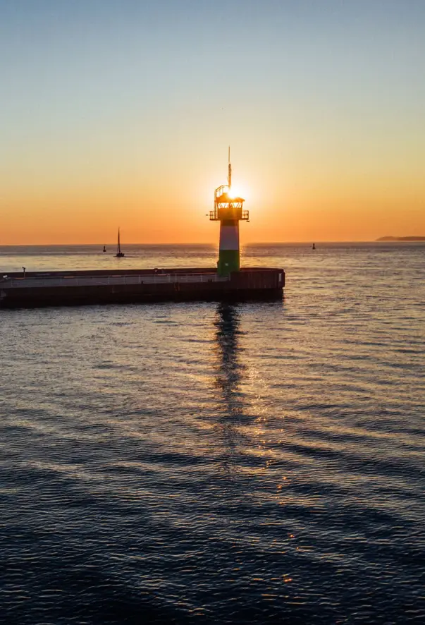 Molo con un faro nell'acqua al tramonto.