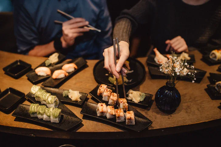 Persona che tiene dei bastoncini di sushi su un piatto.