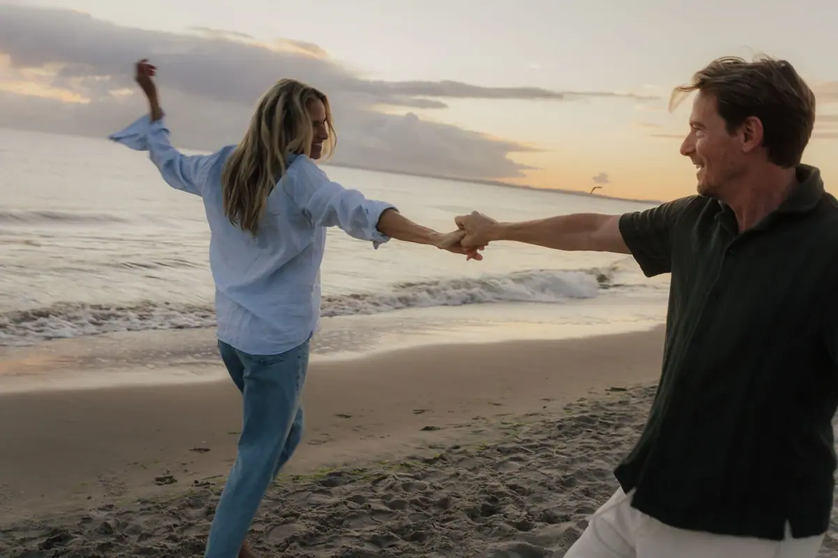Un uomo e una donna si tengono per mano su una spiaggia.