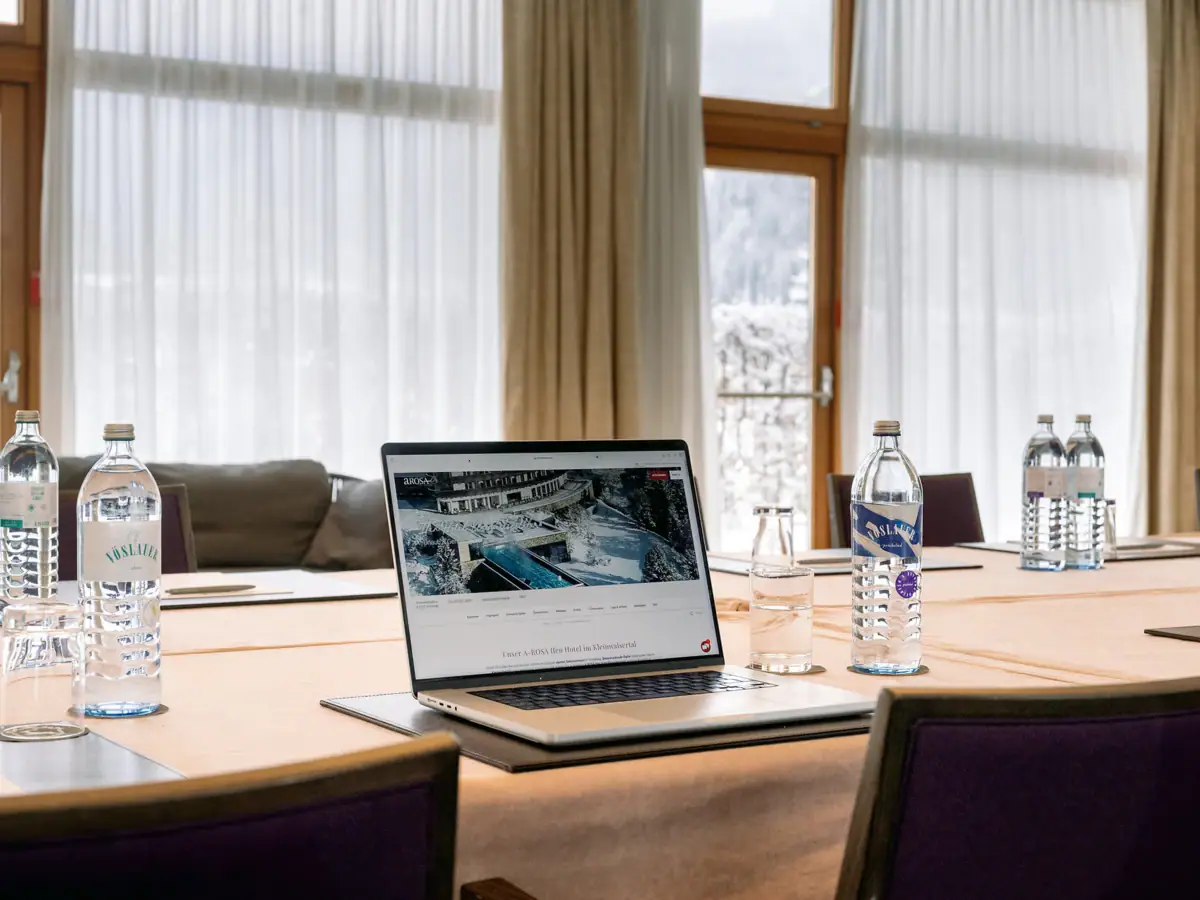 Tagungsraum Ein Laptop auf einem Tisch mit Wasserflaschen und einem Fenster im Hintergrund.
