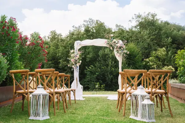 Hochzeitsbogen mit Blumenarrangement und Stühlen im Garten für die Trauung.