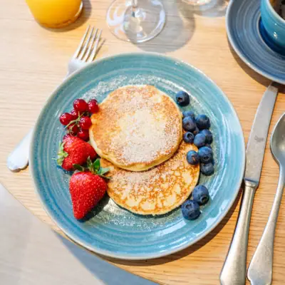 Piatto di pancakes con frutti di bosco e una tazza di caffè.