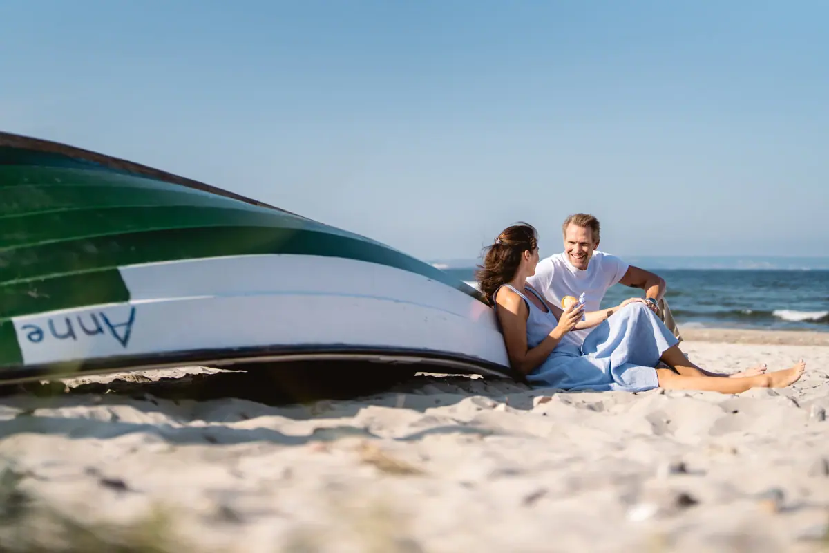 Un uomo e una donna sono seduti sulla spiaggia accanto a una barca.