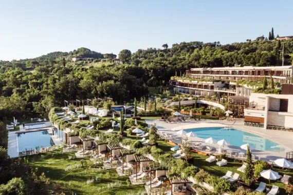 Piscine davanti a un edificio con alberi e una collina sullo sfondo.