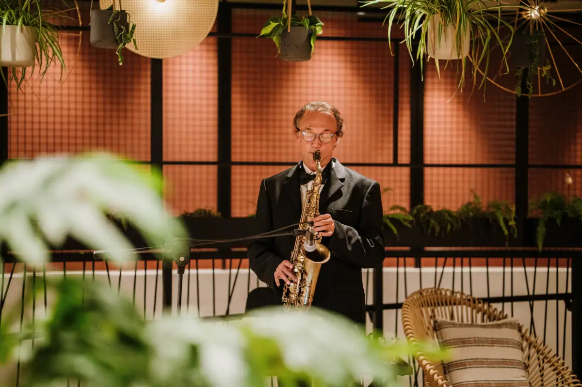 Musica dal vivo nel bar. Musicista con sax che suona dal vivo al bar dell’A-ROSA Lago di Garda, in un’atmosfera elegante e rilassata con dettagli di design e piante verdi.
