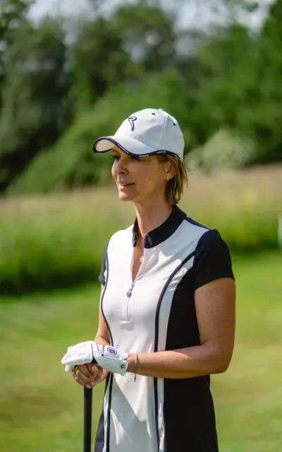 Donna con berretto e camicia bianca in piedi su un prato a giocare a golf.