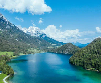 Lago circondato da montagne con alberi e cielo nuvoloso.