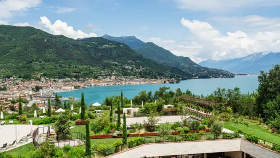 Edificio circondato da un lago e alberi con montagne e nuvole sullo sfondo.