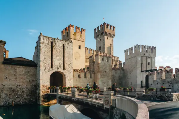 Sirmione Un castello con un ponte e uno specchio d'acqua.