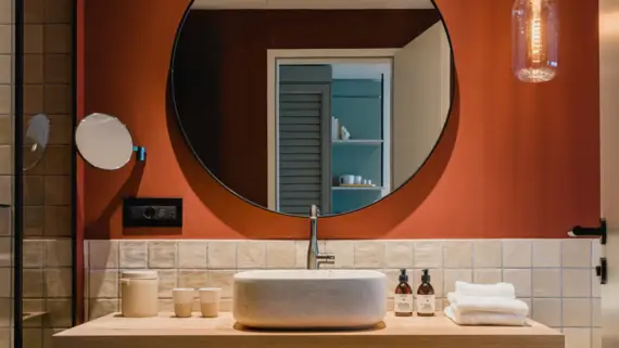 Bagno moderno con specchio rotondo, lavandino, rubinetto e piastrelle chiare.