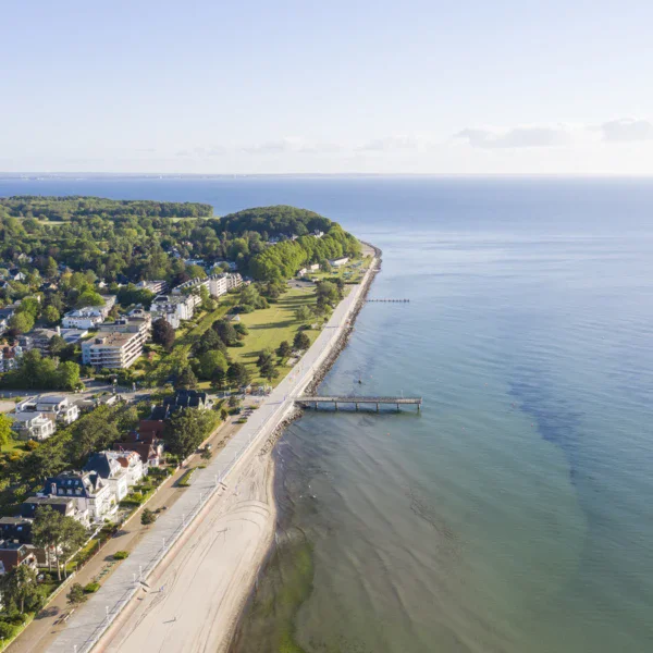 Spiaggia con vista su un corpo d'acqua e una città in lontananza, circondata da vegetazione tropicale.