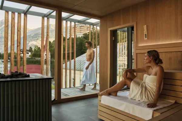 Una donna siede in una sauna con un uomo in accappatoio bianco.