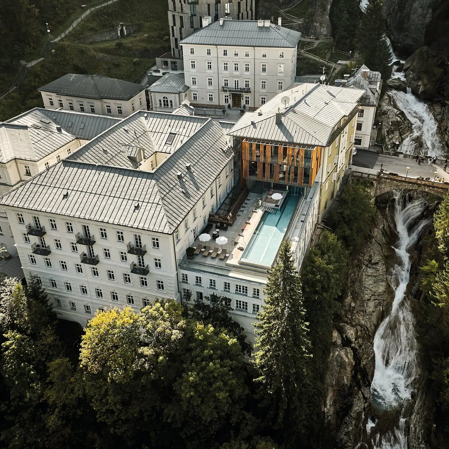 Un edificio con piscina e cascata esterna, circondato da alberi.