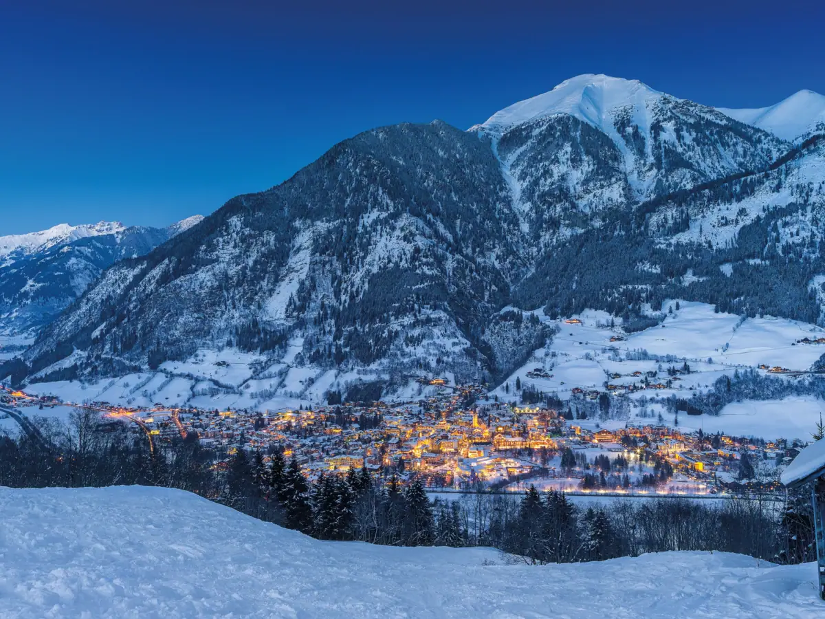 Luci cittadine nella neve in un paesaggio montano invernale.