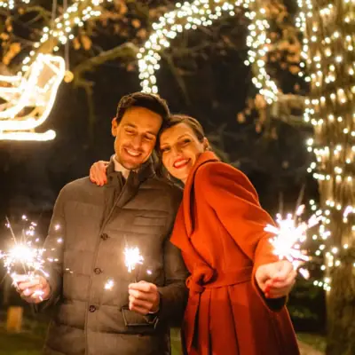 Un uomo e una donna che tengono scintille davanti a luci decorative.