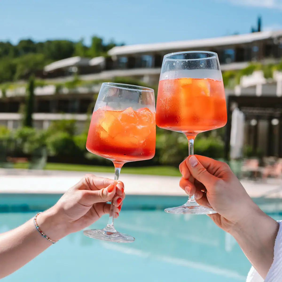 Ein Paar Hände hält Gläser mit Aperol und Eis gefüllt. 