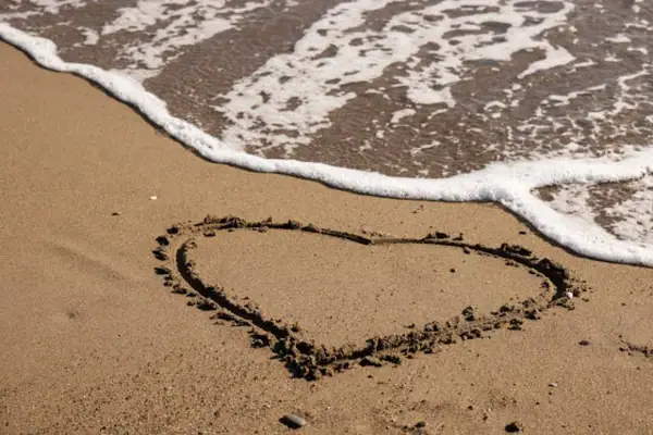 Ein Herz im Sand neben einer Welle.