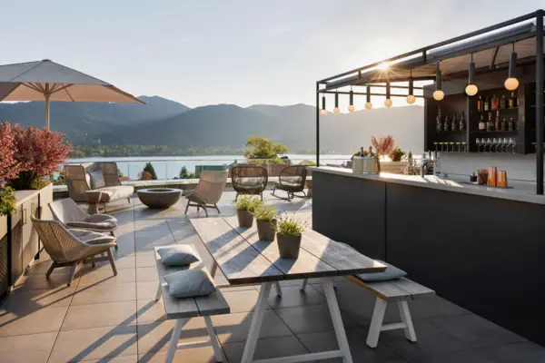La terrazza dell’A-ROSA Tegernsee, con un bar e tavolini, offre una vista spettacolare sul lago Tegernsee e sulle montagne.