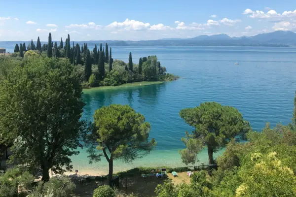 Il limpido lago di Garda con gli alberi sotto un cielo nuvoloso.