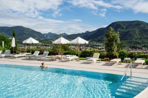 Persona in piscina circondata da ombrelloni e sedie a sdraio.