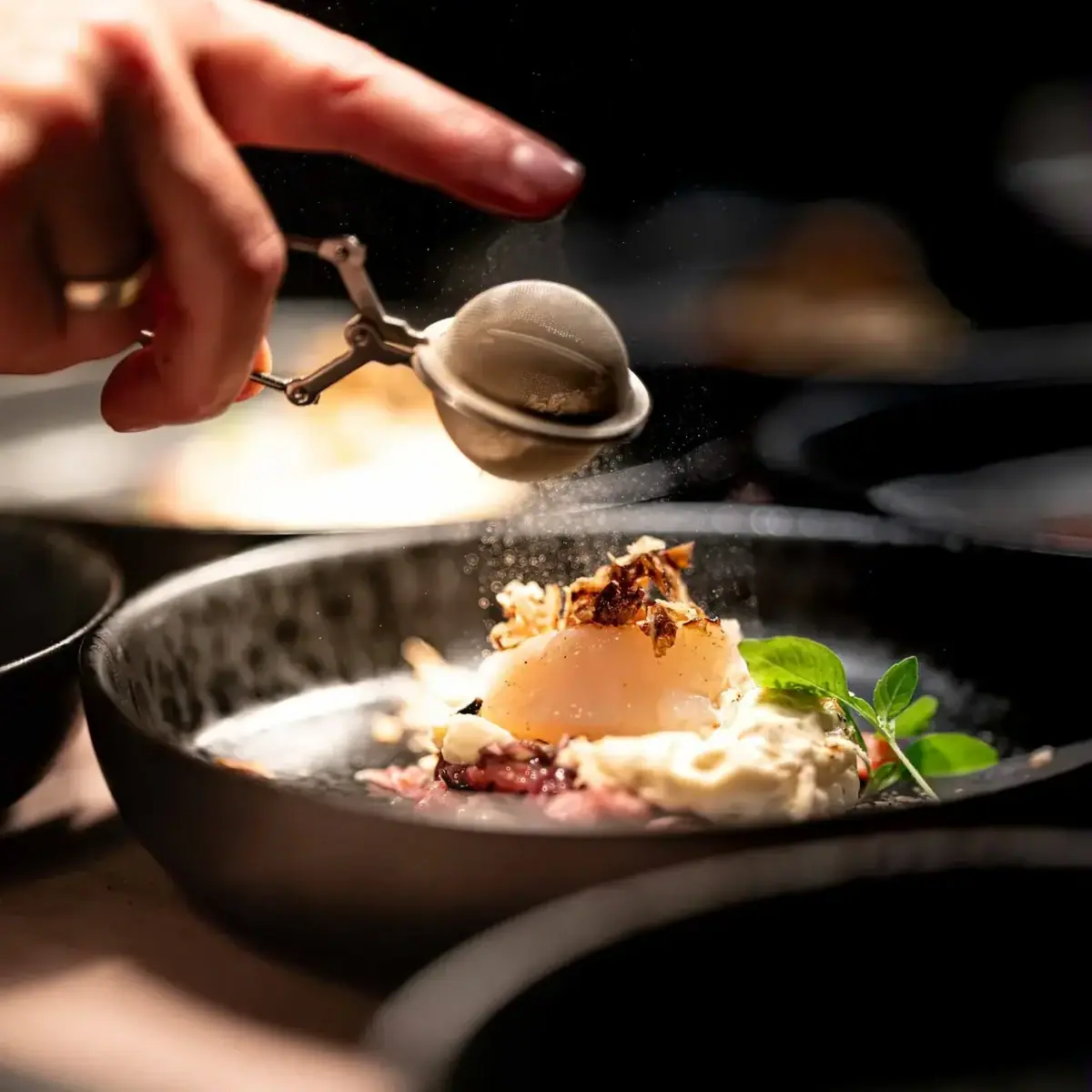 Una mano spolvera uno zucchero a velo su un dessert in un piatto.