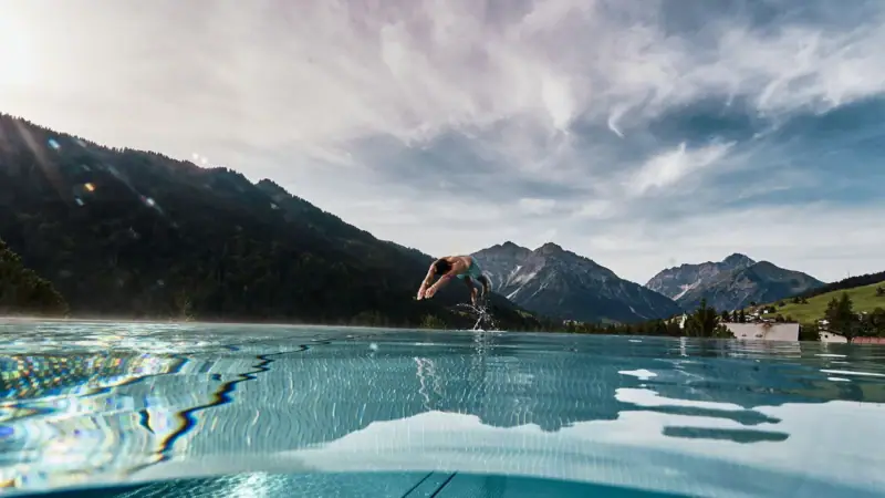 Persona che salta in una piscina con montagne sullo sfondo.
