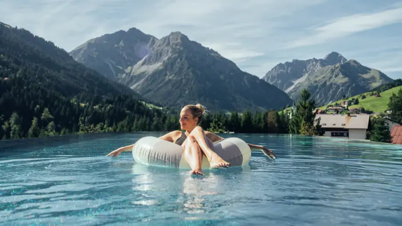 Donna che galleggia su un tubo in una piscina con montagne sullo sfondo.