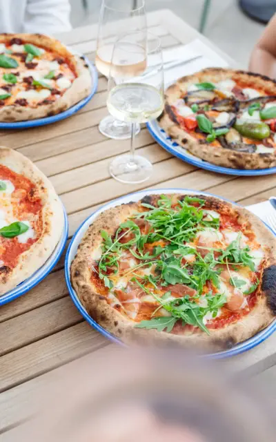 Un tavolo con quattro pizze e bicchieri di vino. 