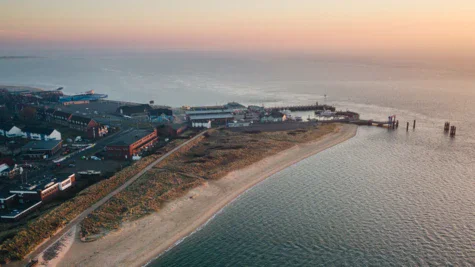 Una spiaggia con edifici e un corpo d'acqua, circondata da un paesaggio costiero al tramonto.