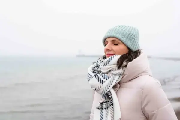 Frau im Winter am Meer Eine Frau mit Hut und Schal steht am Wasser.