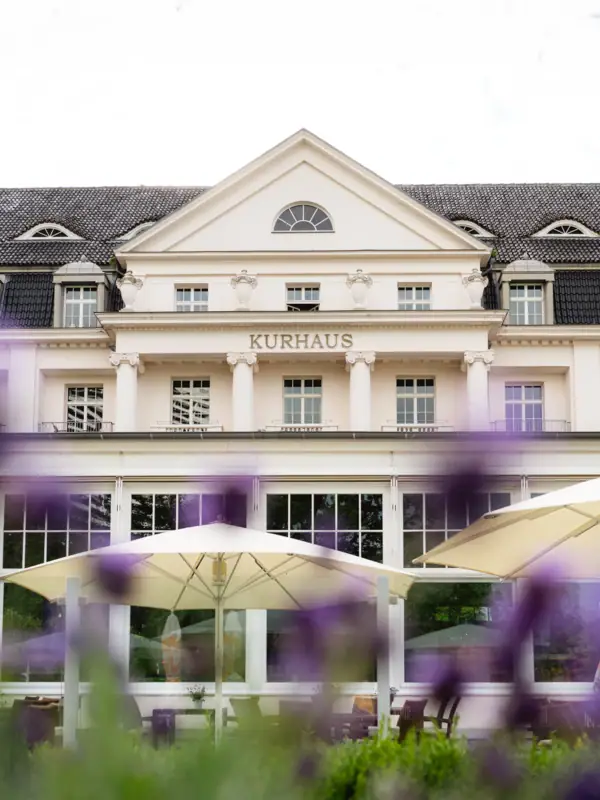 A-ROSA Travemünde Ein Gebäude mit großen Fenstern, der Aufschrift "Kurhaus" und einem großen Sonnenschirm.