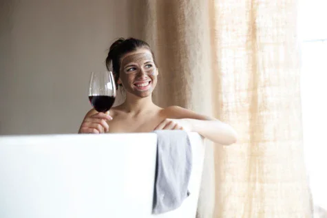 Donna sorridente in una vasca da bagno con un bicchiere di vino.