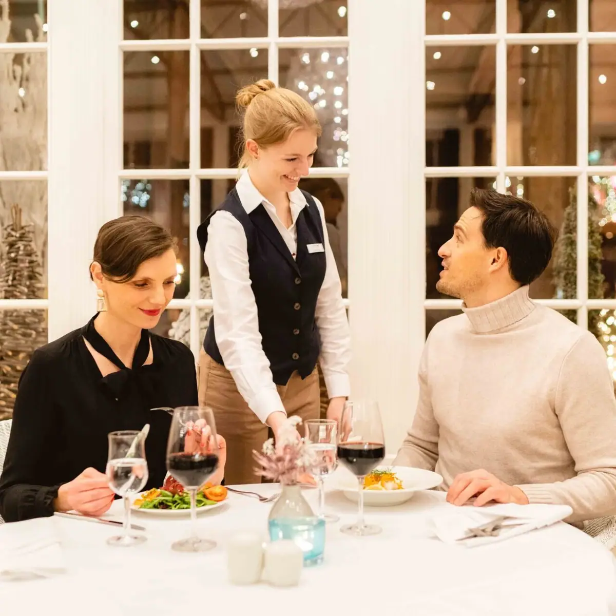 Natale A-ROSA Un gruppo di persone sedute attorno a un tavolo apparecchiato con bicchieri di vino.