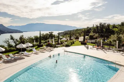 Vista aerea di una lussuosa piscina all'aperto con persone che nuotano e lettini intorno. 