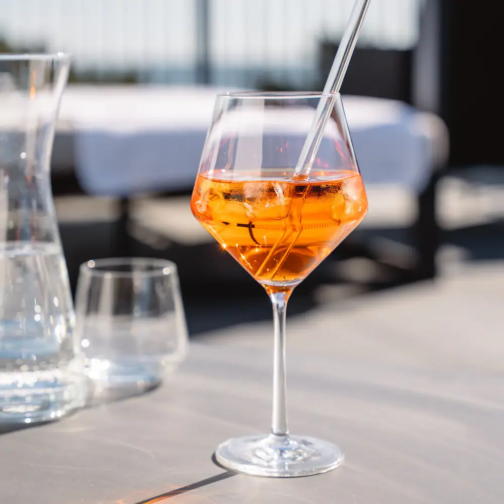 Ein Glas mit orangefarbener Flüssigkeit und Eis auf einem Tisch.