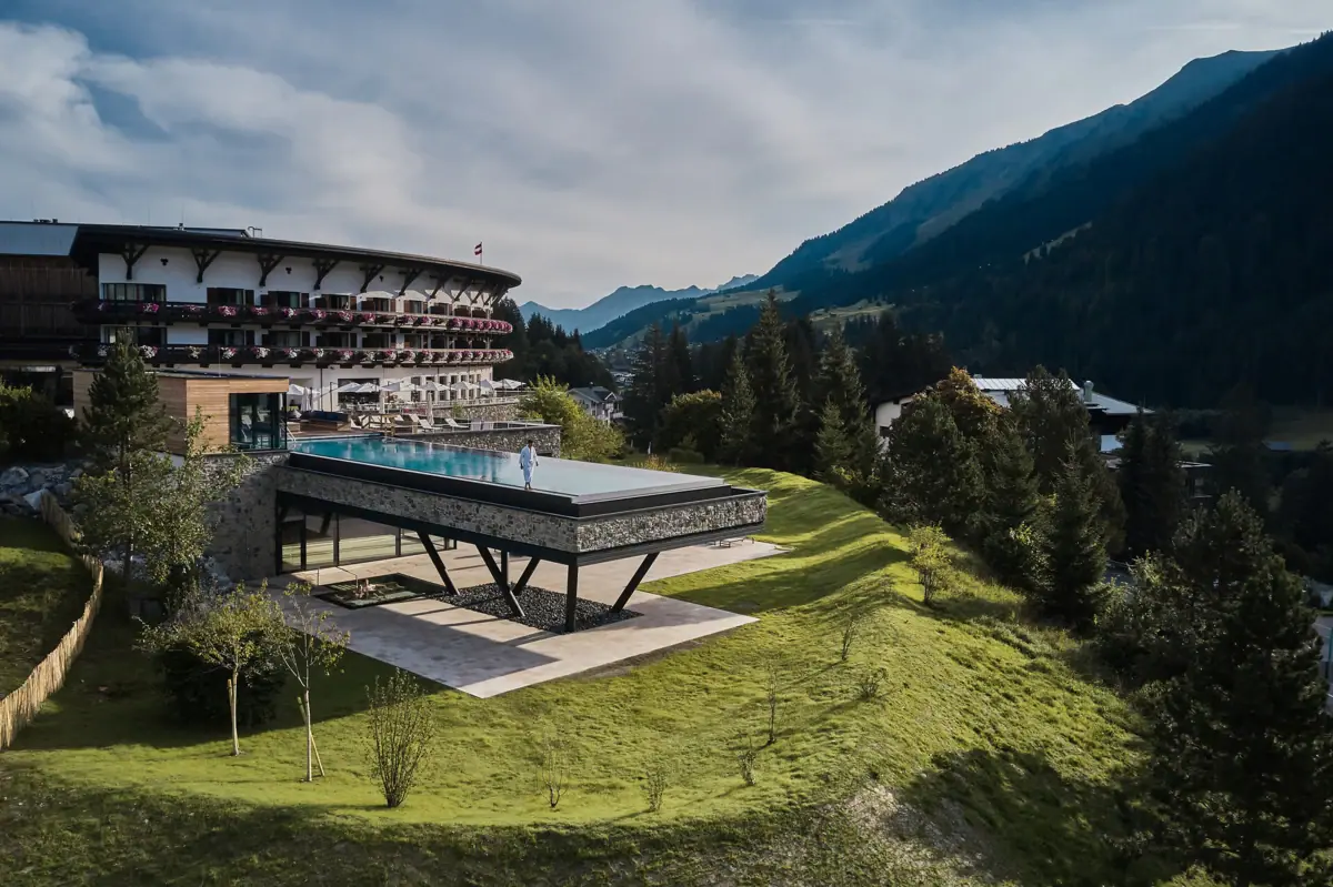 Un edificio con una piscina al centro, circondato dalle montagne e dal cielo azzurro.